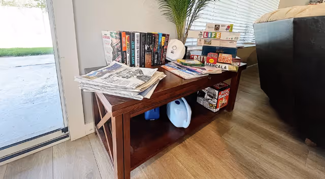 Wooden console table with magazines, newspapers, and board games in a cozy living area.