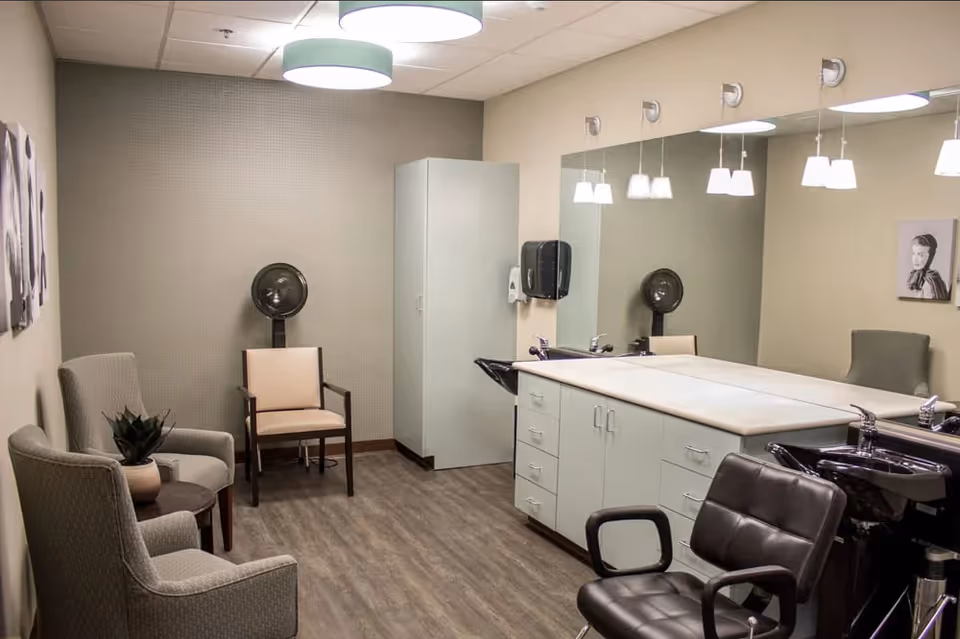 A clean salon room with styling chairs, shampoo sinks, large mirrors, cabinetry, and waiting chairs.