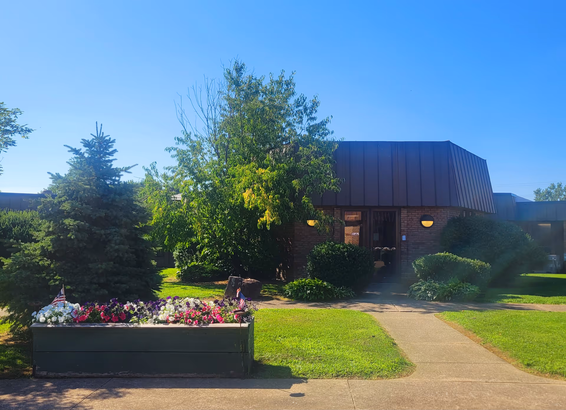Exterior view of a brick facility with a metal roof and landscaped flower bed.