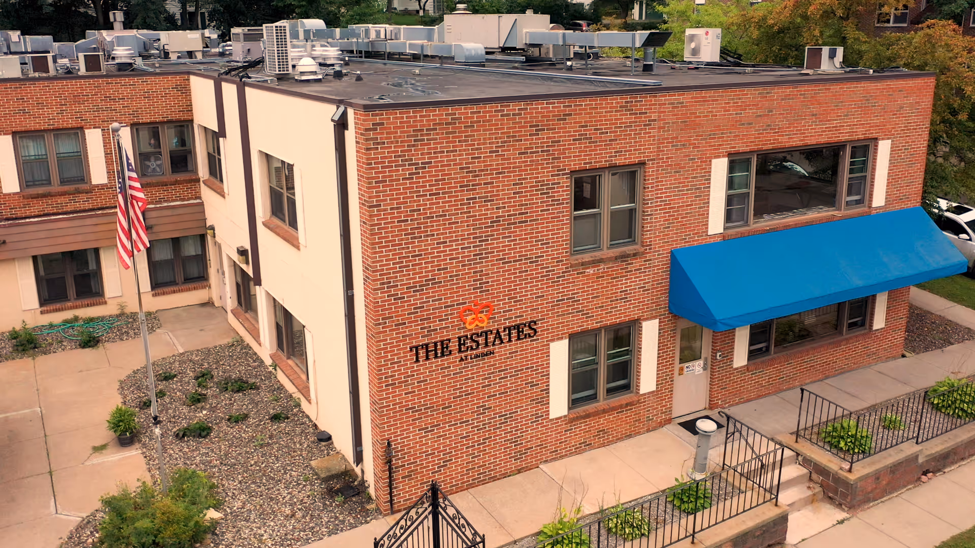 Brick two-story building front with a blue awning over the entrance and a sign reading "THE ESTATES".