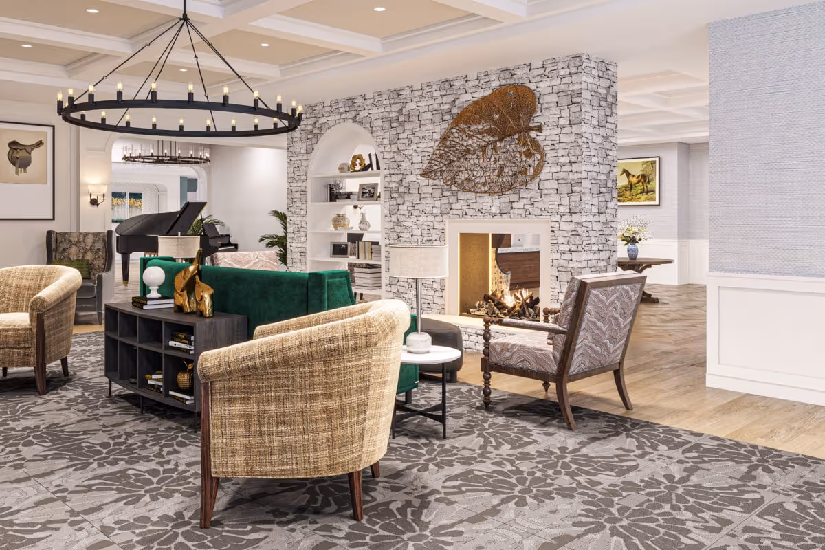Comfortable communal living room with armchairs and a green sofa arranged around a fireplace, piano, and large chandelier.