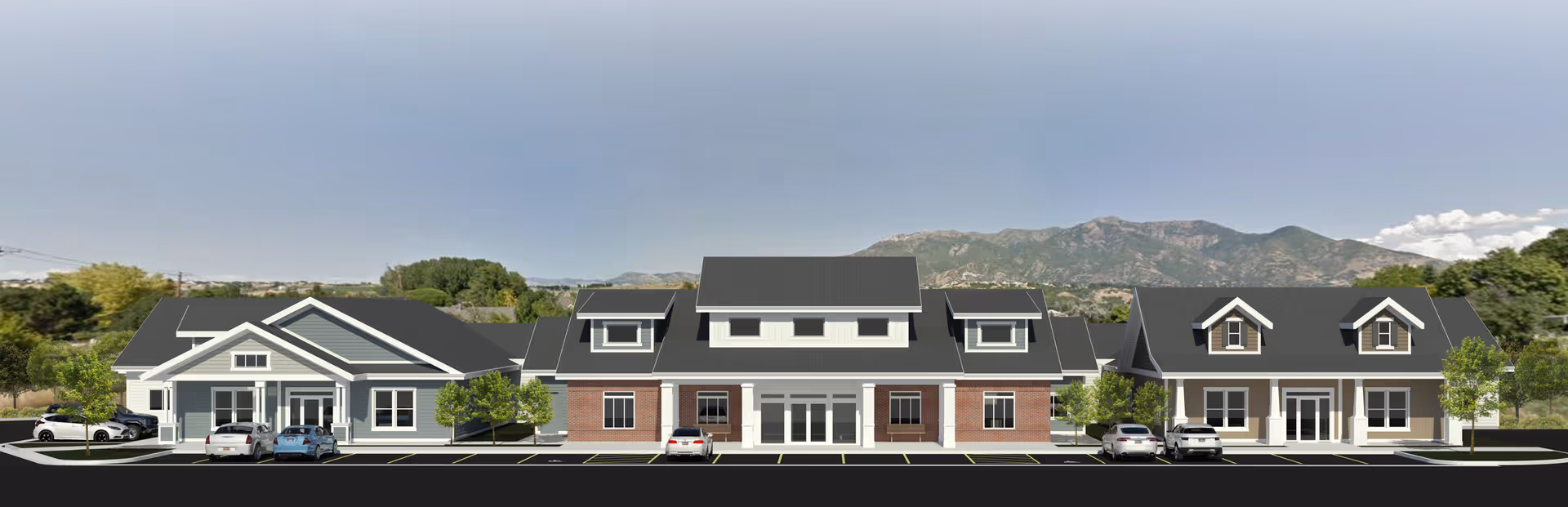 Front exterior view of Petersen Farms Assisted Living facility showing a single-story building with three connected sections. The building features a combination of brick and siding exteriors with multiple windows and entrances. Several cars are parked in front, and there are small trees and landscaping around the parking area. Mountains and a clear sky are visible in the background.