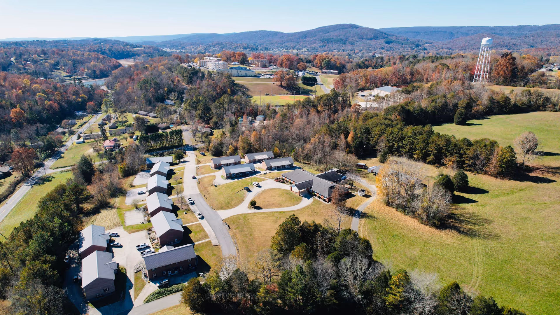 Aerial view of a senior living campus with multiple single-story residential buildings, driveways, open lawns and surrounding hills.