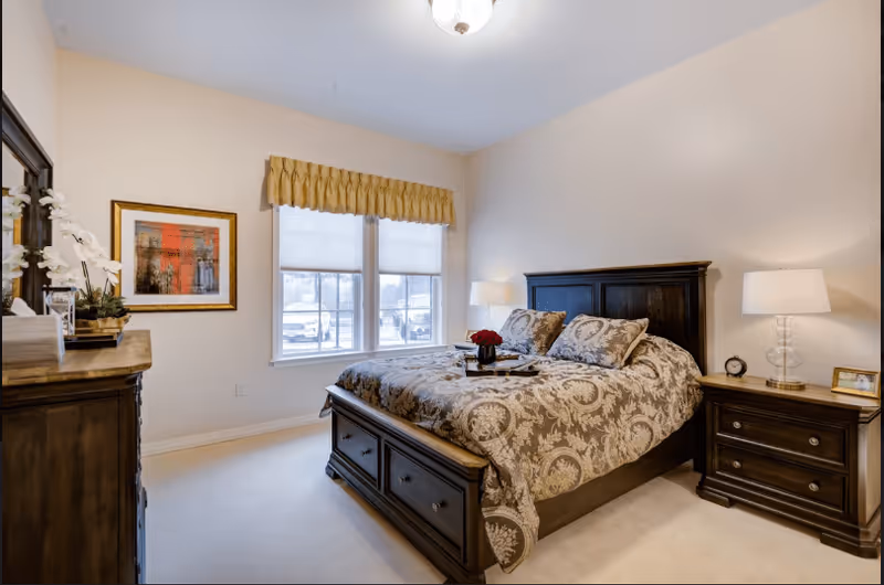 Bright, neatly staged bedroom with a dark wood bed and matching nightstands, patterned bedding, dresser, and a window with a valance.