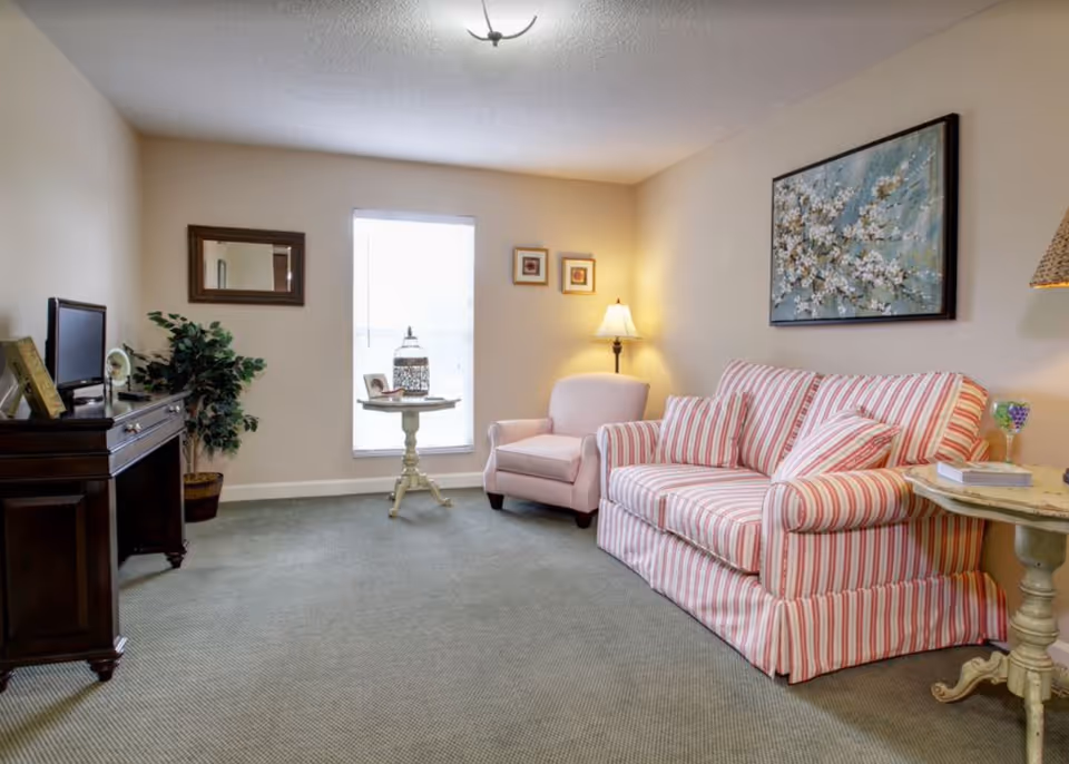 Well-lit living room with a striped sofa and matching armchair, side tables, a TV stand, and wall art.