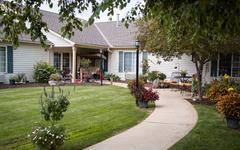 Well-maintained courtyard with a curved concrete path, green lawn, potted flowers, patio seating and the building's exterior.
