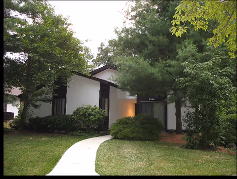 White, single-story senior living building with curved walkway amid trees.