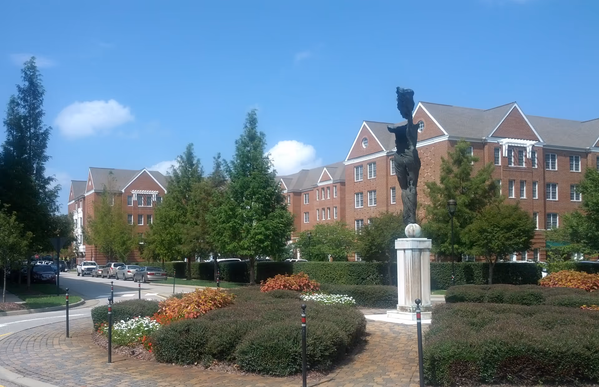 Brick senior living campus visible with a statue and manicured circular driveway.