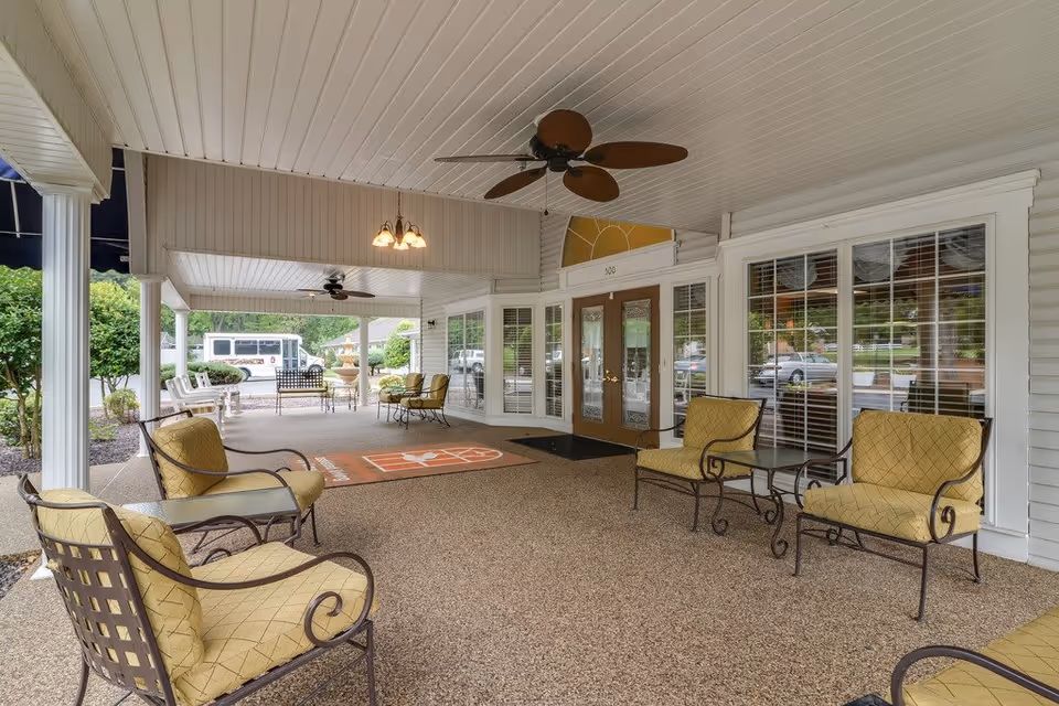 Covered front entrance patio with cushioned seating, ceiling fans, and double glass doors.