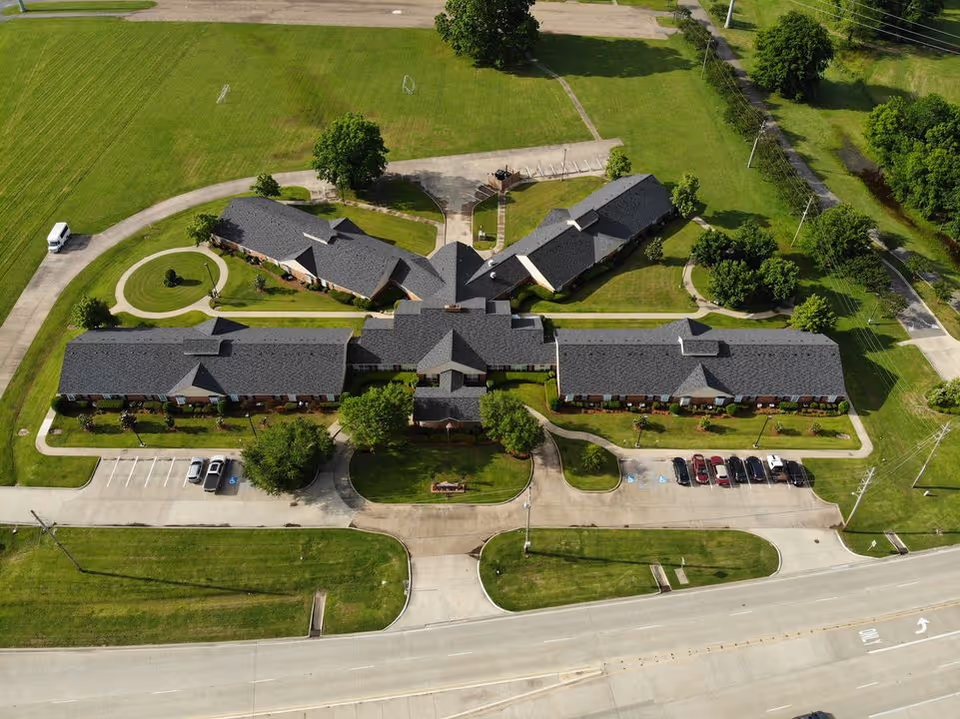 Aerial view of Azalea Estates of Shreveport, showing a large single-story building complex with multiple wings surrounded by green lawns, trees, parking spaces, and adjacent roads.