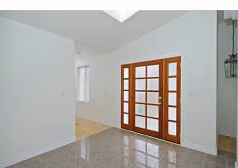 Interior view of a room with white walls, a polished tile floor, and a wooden framed glass door. There is a skylight on the ceiling and a window on the left side wall.