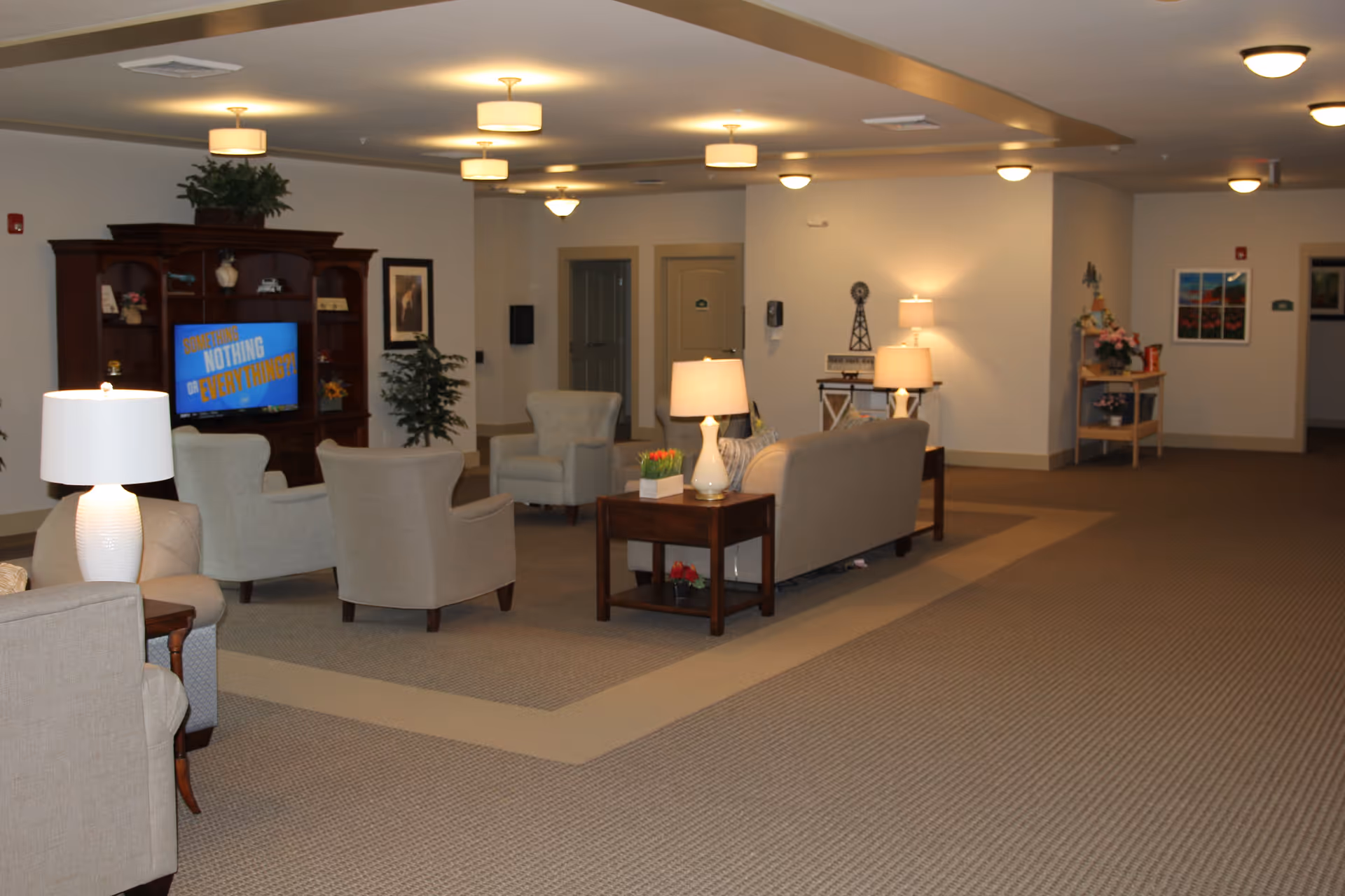 Spacious communal lounge with sofas and armchairs arranged around side tables and lamps, a TV cabinet, and decorative accents.