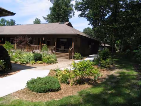 Single-story lodge-style building with a wooden porch, landscaped garden, and curved walkway.
