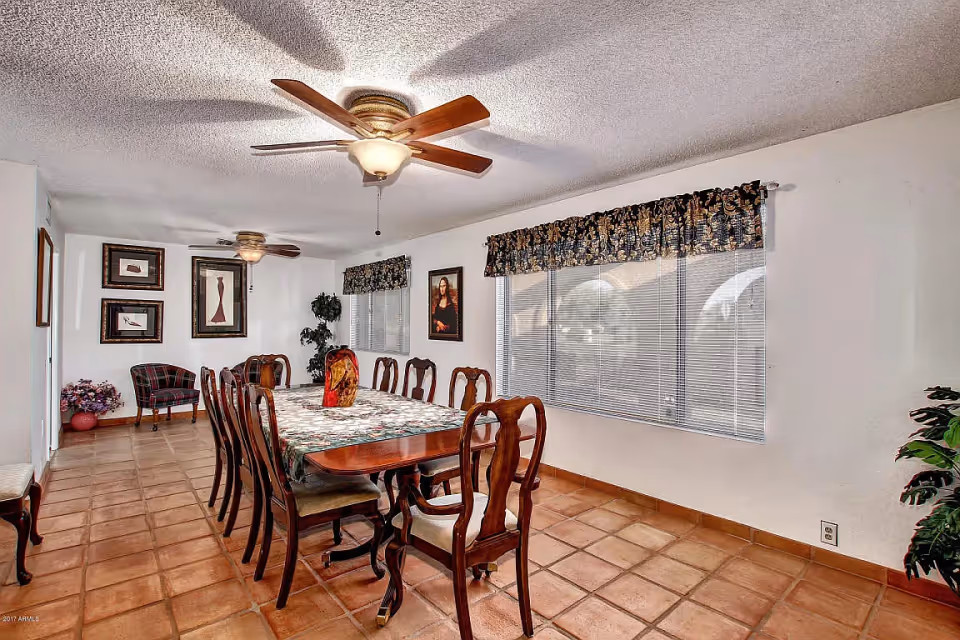 Formal dining room with a long wooden table and chairs, ceiling fans, tiled floor, and large windows with valances.