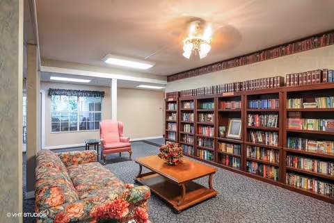 Cozy lounge/library with built-in bookshelves, a floral sofa, pink armchair and wooden coffee table.