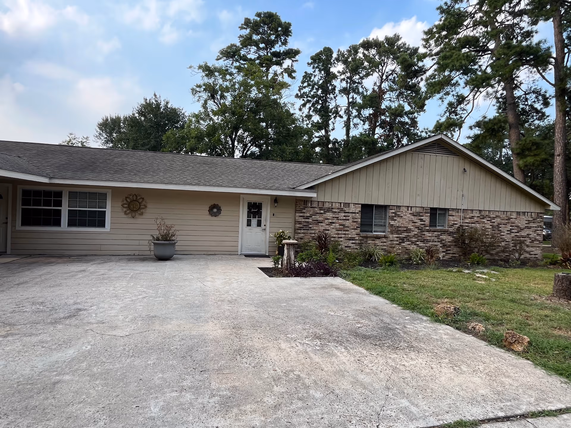 Single-story facility exterior with driveway, beige siding, brick accents, and tall pine trees.
