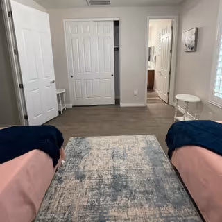 Two twin beds with pink covers flank a central rug in a shared bedroom.