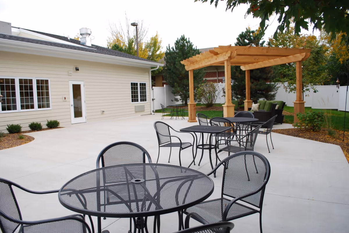 Outdoor patio with metal tables and chairs and a wooden pergola next to a light-colored building.