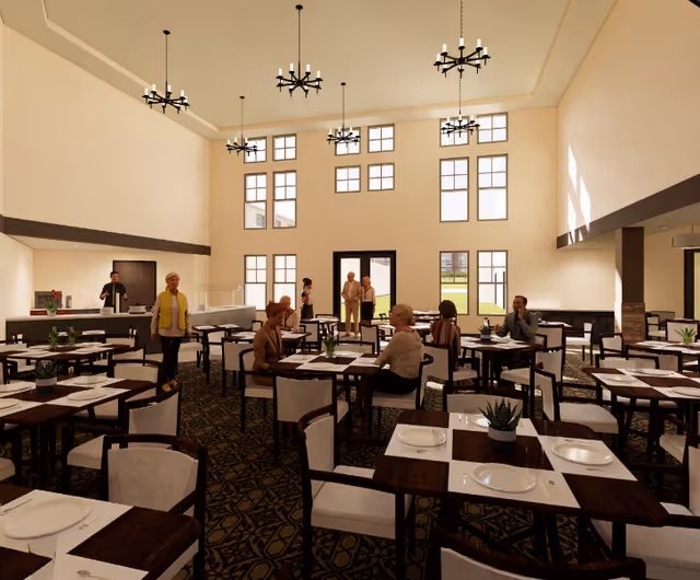 A spacious dining room in a senior living facility with high ceilings and large windows letting in natural light. Several elderly people are seated at tables, engaging in conversation, while a few others stand near the entrance and serving area. The room is furnished with dark wooden tables and cushioned chairs, each table set with plates, utensils, and small potted plants as centerpieces. Modern chandeliers hang from the ceiling.