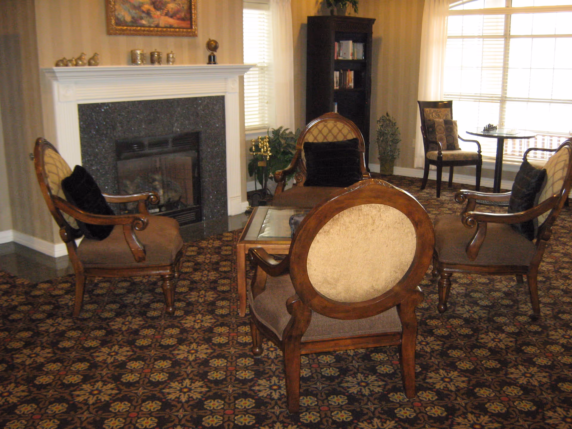 A cozy living room with upholstered wooden chairs arranged around a glass coffee table in front of a fireplace.