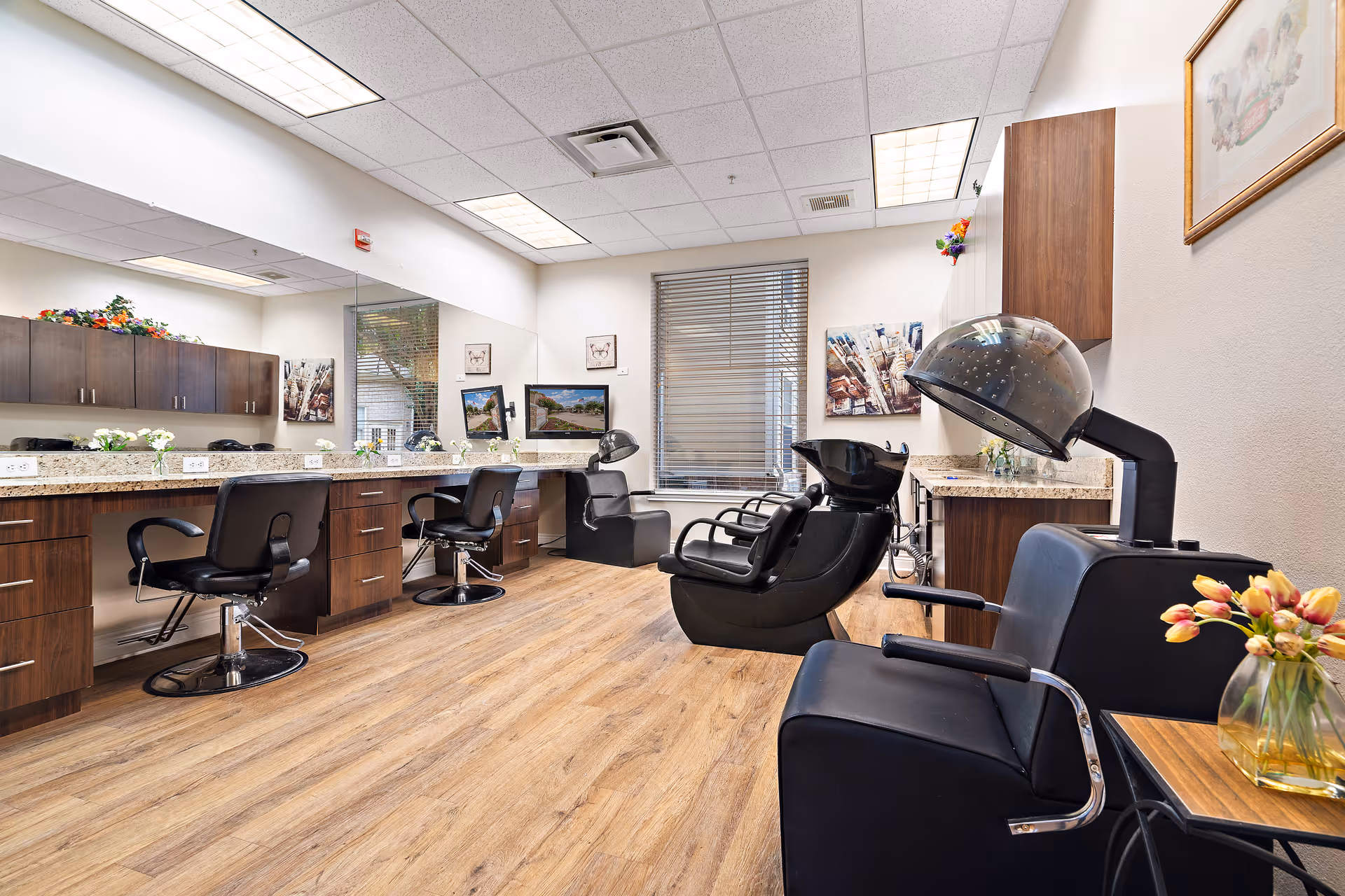 Salon room with styling chairs, mirrors, shampoo sinks, hooded hair dryers, and wood-look flooring.