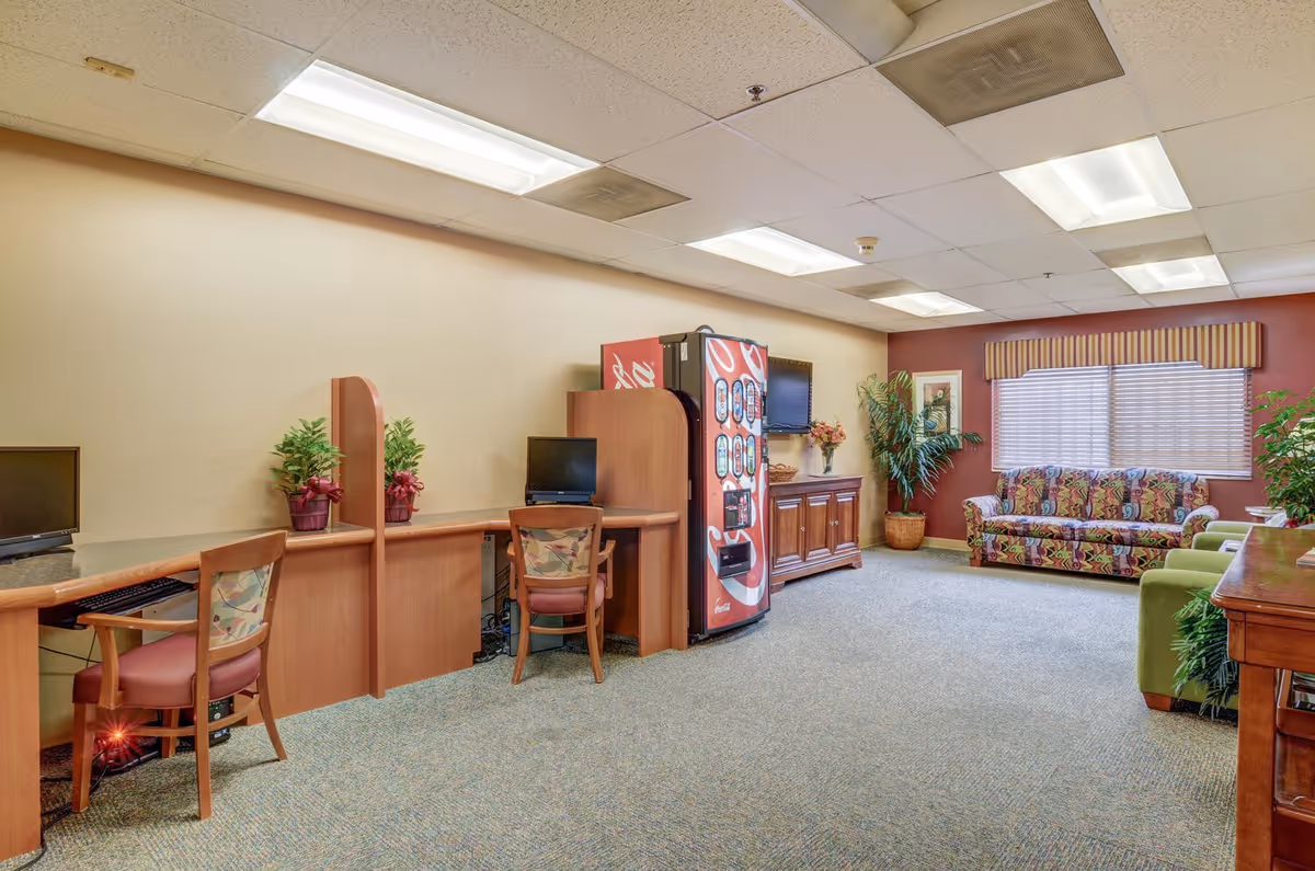 Bright common room with computer workstations, a soda vending machine, and upholstered sofas and chairs.