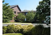 Brick senior living facility building front with landscaped shrubs, trees, and a small statue near the entrance.