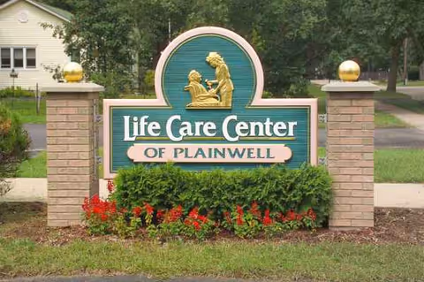 Sign for Life Care Center of Plainwell between two brick pillars topped with gold spheres.