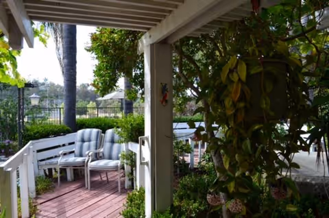 Outdoor covered seating area with white chairs and lush plants at Brandon Manor