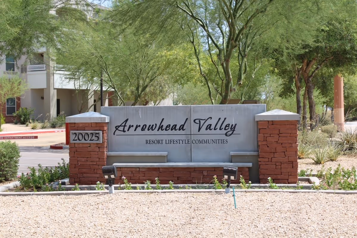 Outdoor view of the entrance sign for Arrowhead Valley Resort Lifestyle Communities, featuring a stone and concrete structure with the address number 20025, surrounded by desert landscaping and trees.