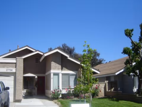 Front exterior of a single-story residential building with a driveway, lawn, and trees.