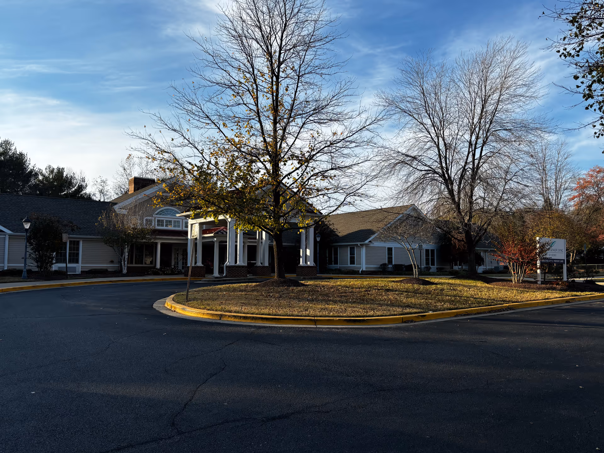 Exterior view of Charter Senior Living Of Bowie building with a circular driveway, leafless trees, and a clear blue sky.