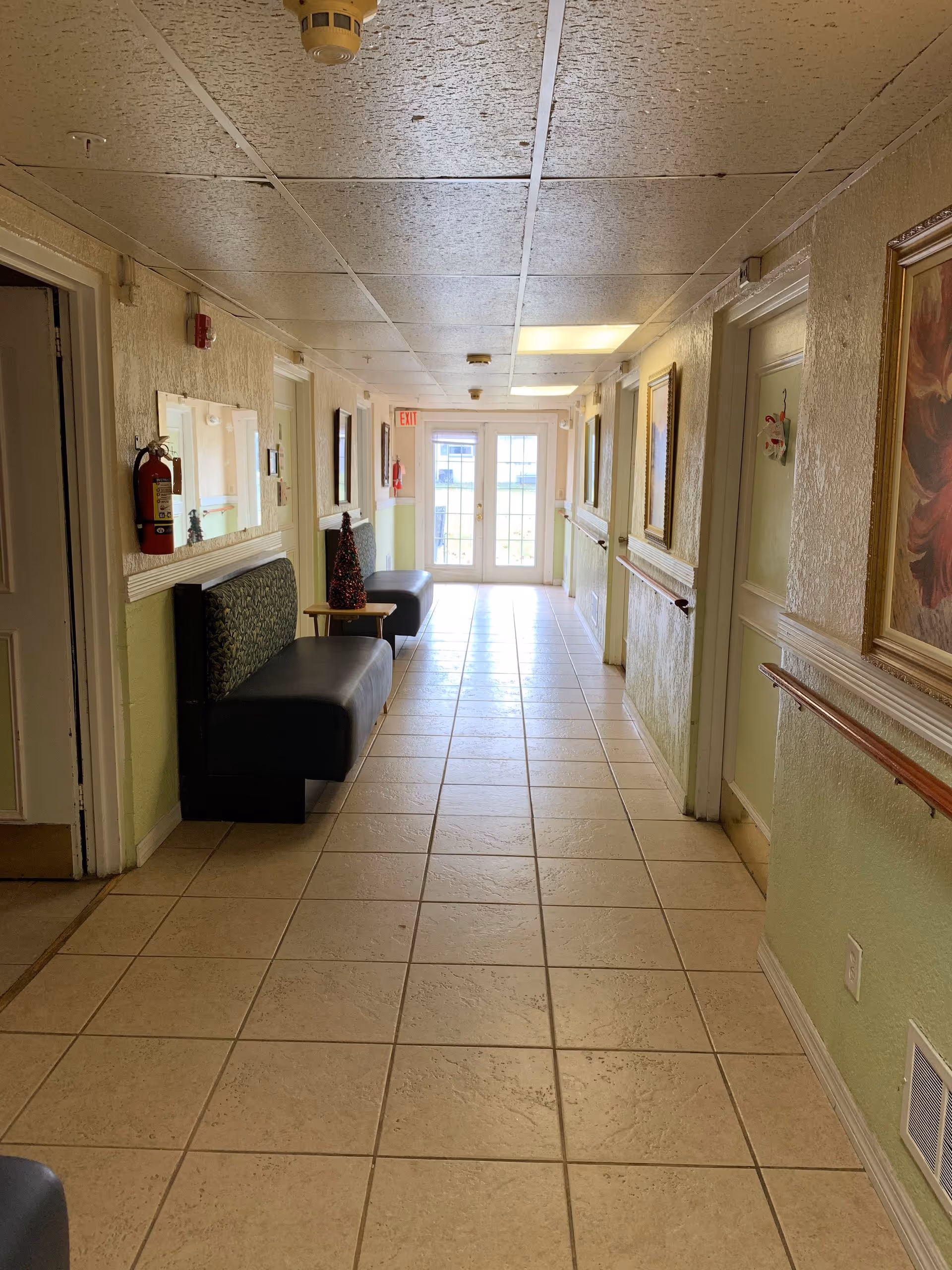 Long interior hallway of a senior living facility with benches and framed artworks.