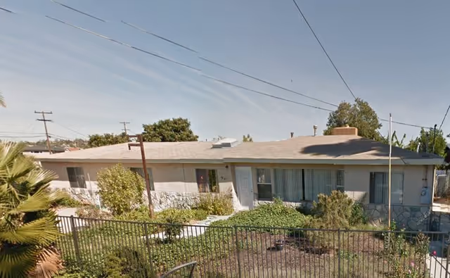Exterior view of a single-story senior care facility with shrubs behind a metal fence.