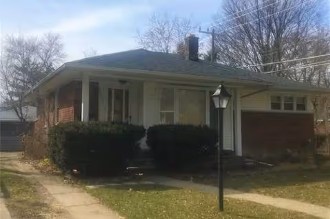 Single-story house with front porch, hedges, and a lamppost outside.
