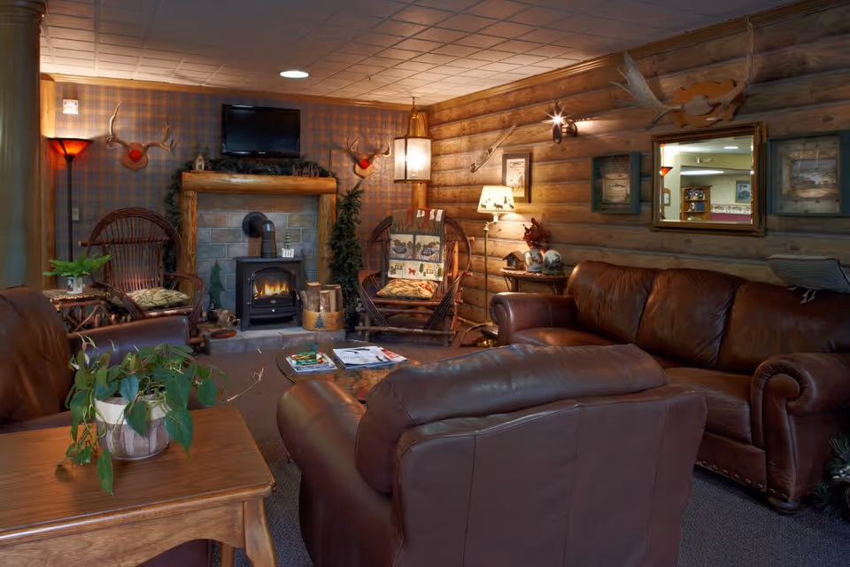 Cozy rustic lounge with leather sofas, a small fireplace, wicker chairs, and wood-paneled walls.