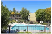 Fenced outdoor swimming pool with lounge chairs and landscaping in front of a two-story residential building.