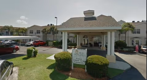 Front entrance of Belvedere Commons of Sun City Center showing a covered porte-cochere, parking, and a landscaped sign at the driveway.