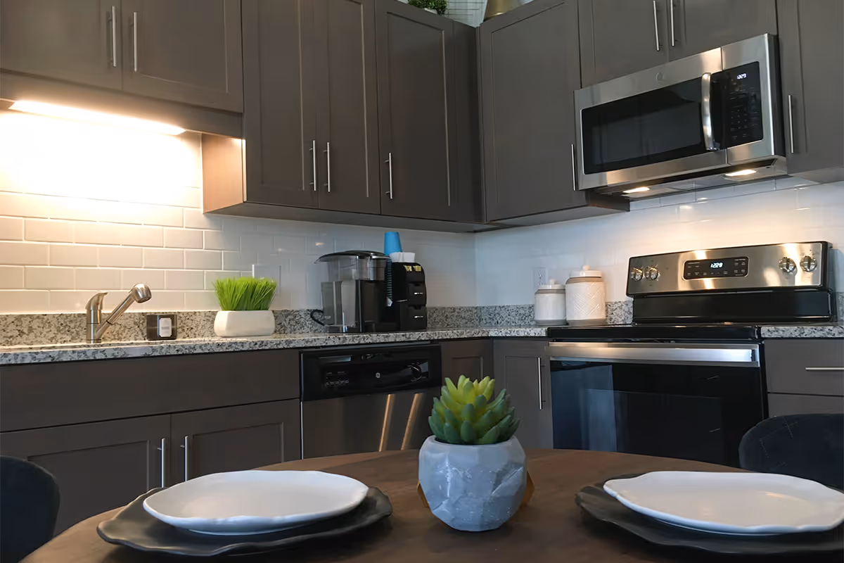 Modern kitchen with gray cabinets, stainless steel appliances, granite countertops and a small dining table set with plates and a succulent.