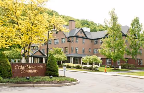 Brick senior living building with trees and Cedar Mountain Commons entrance sign.