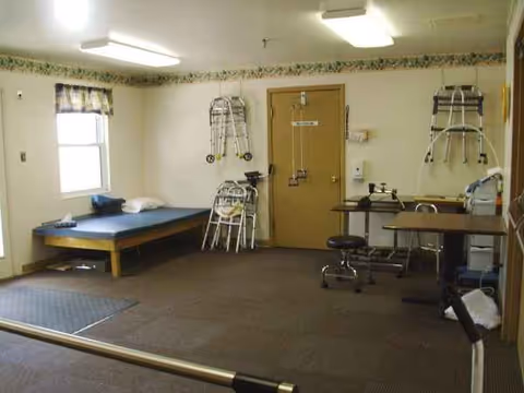 A small rehab room with a bed, walkers on walls, parallel bars, and a workstation.