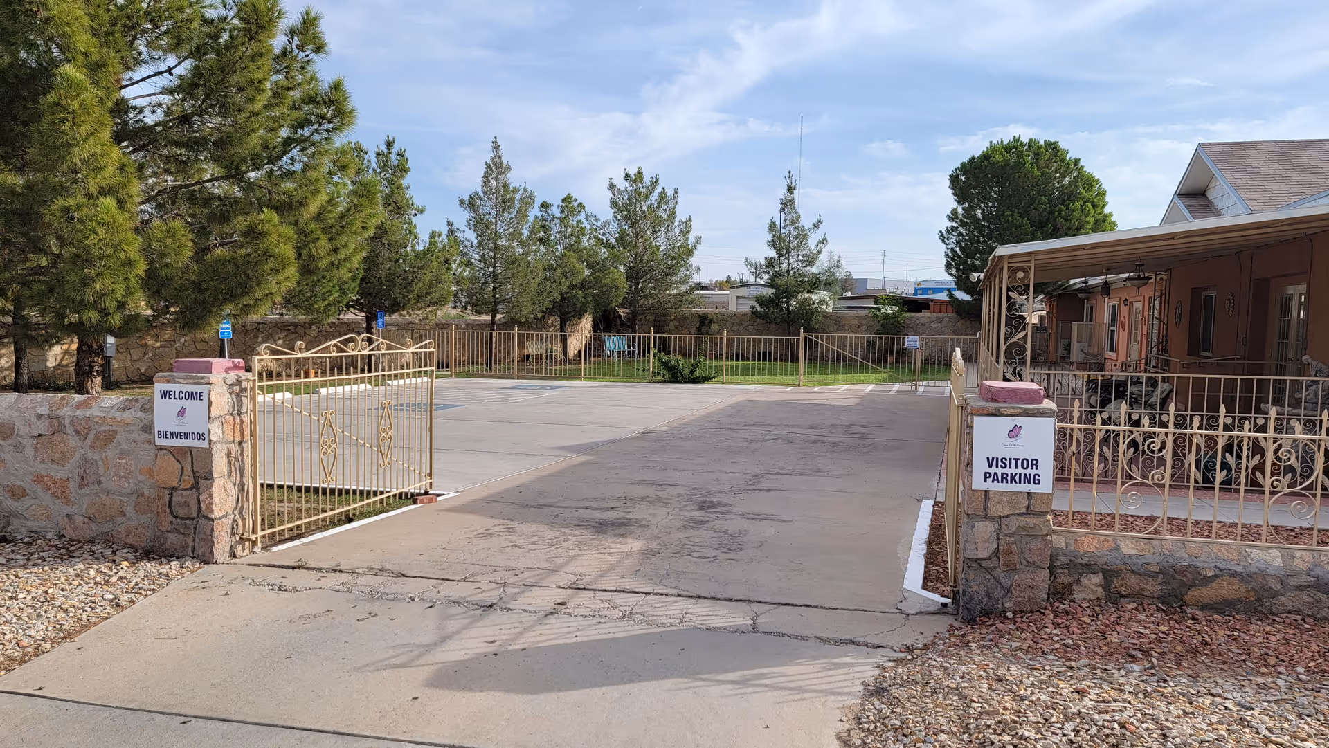 Gated entrance and driveway leading to a parking area and covered porch at an assisted living home with visitor parking signs.