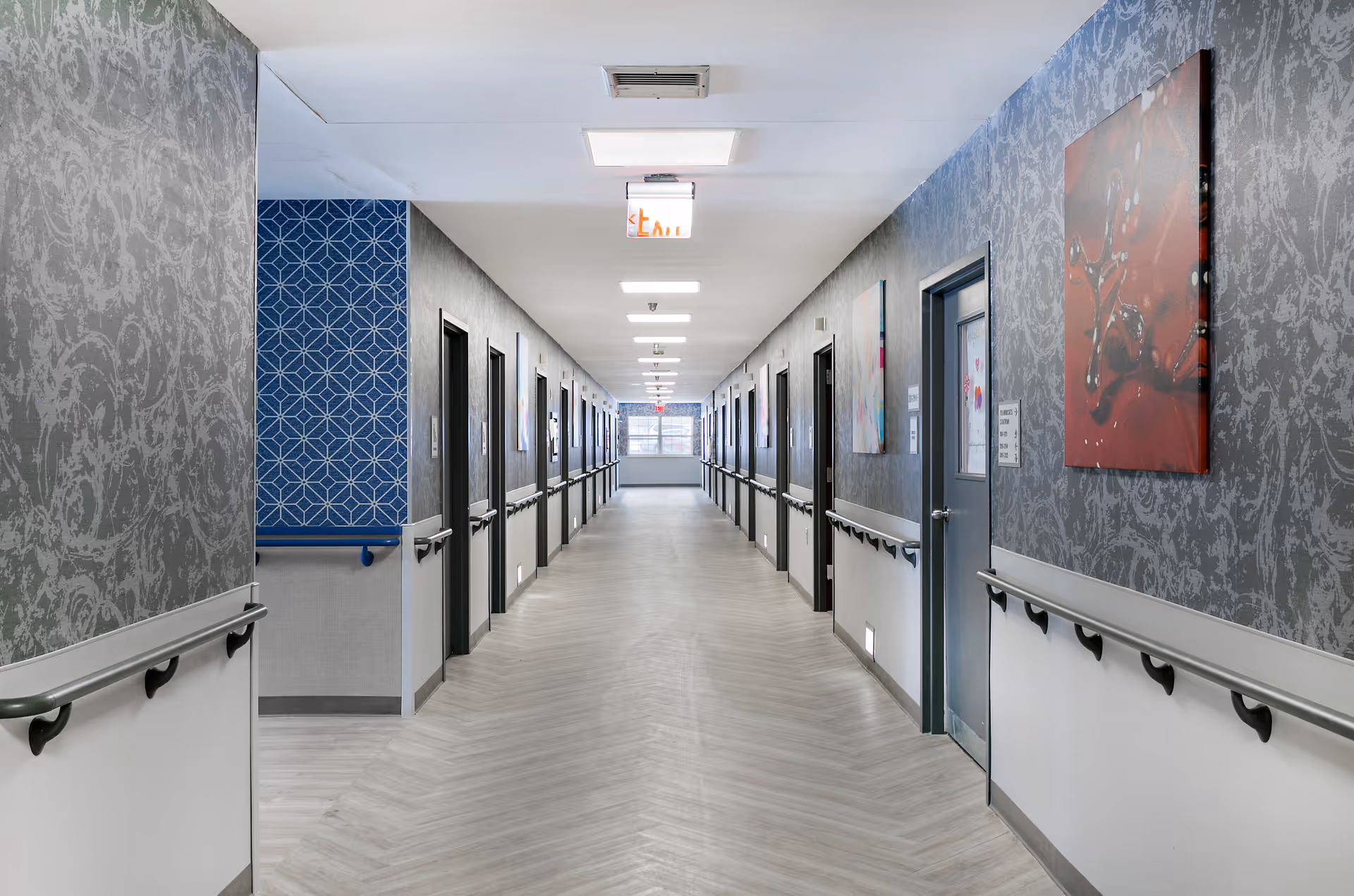 Long, well-lit interior hallway with handrails and doors on both sides in a senior living facility.