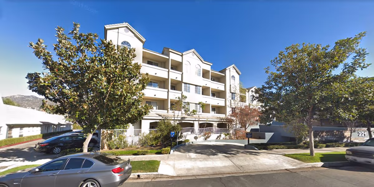 Exterior view of a multi-story senior assisted living facility named Glen Terra Senior Assisted Living, with balconies, trees, parked cars, and a clear blue sky.