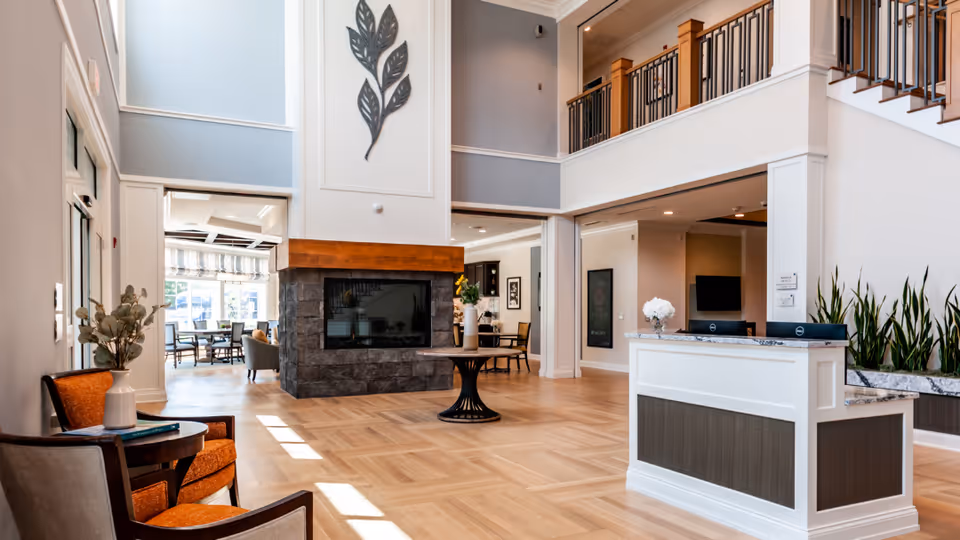 Bright two-story lobby with a central stone fireplace, seating area, and a reception desk.