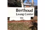 White roadside sign reading "Berthoud Living Center 855" with grass, trees, and a building visible behind it.