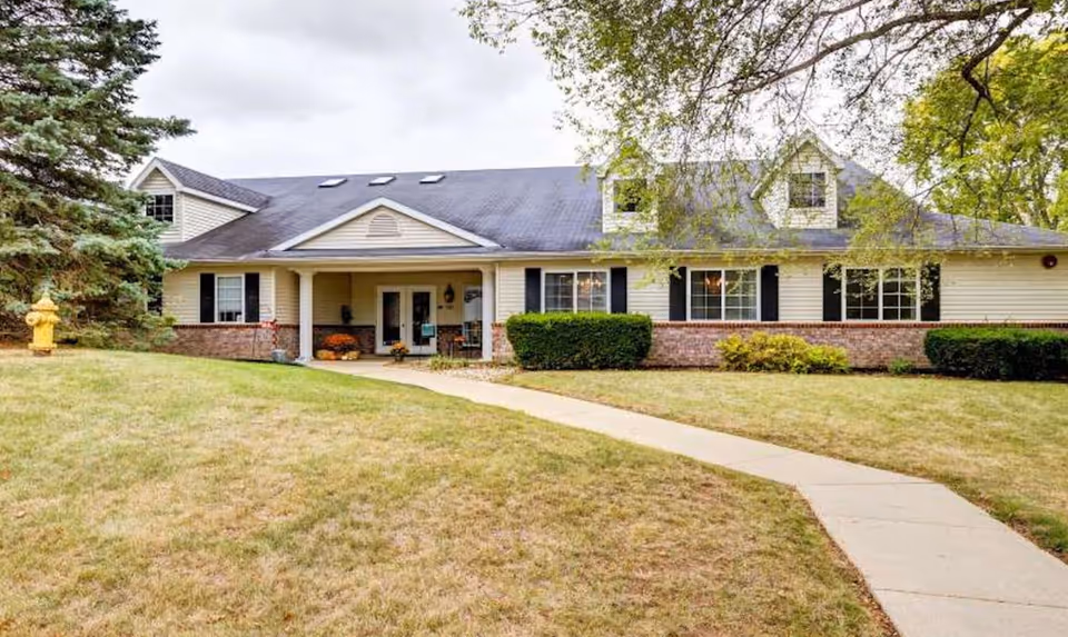 Single-story senior living facility exterior with curved walkway, lawn, and welcoming entrance.