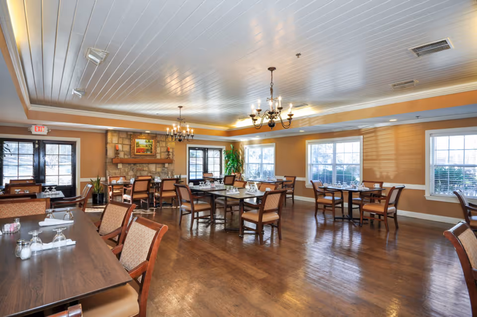 Bright dining room with wooden tables and chairs, chandeliers, and a stone fireplace.
