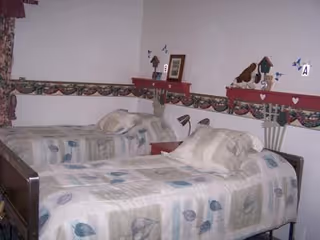 Two twin beds with patterned quilts in a small bedroom with a decorative wall border.