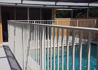 Outdoor pool area with white railings beside a building under a shaded cover.